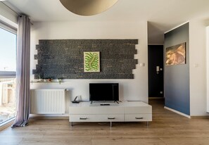 A modern living room with a stone wall, a flat-screen TV, a white console, and a window with curtains. - Stary Browar Deluxe Apartment (Poznań)