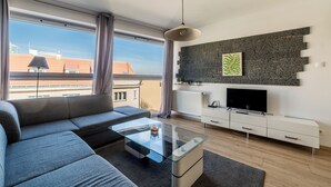 A modern living room with a sectional sofa, a glass coffee table, a flat-screen TV, a stone accent wall, and a view of the cityscape through large windows.