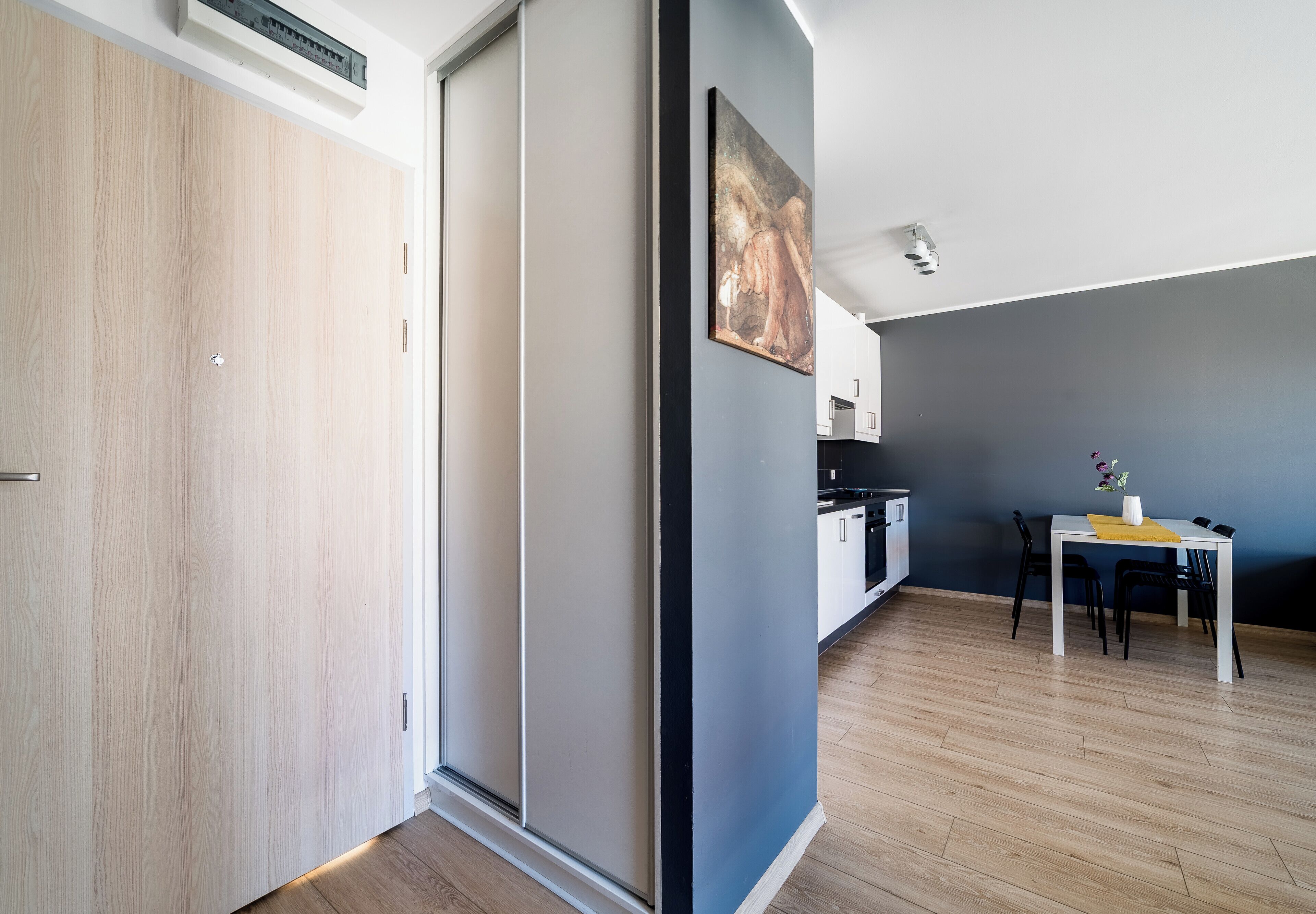 A modern kitchen with white cabinets, a dining table with chairs, and a painting on the wall.