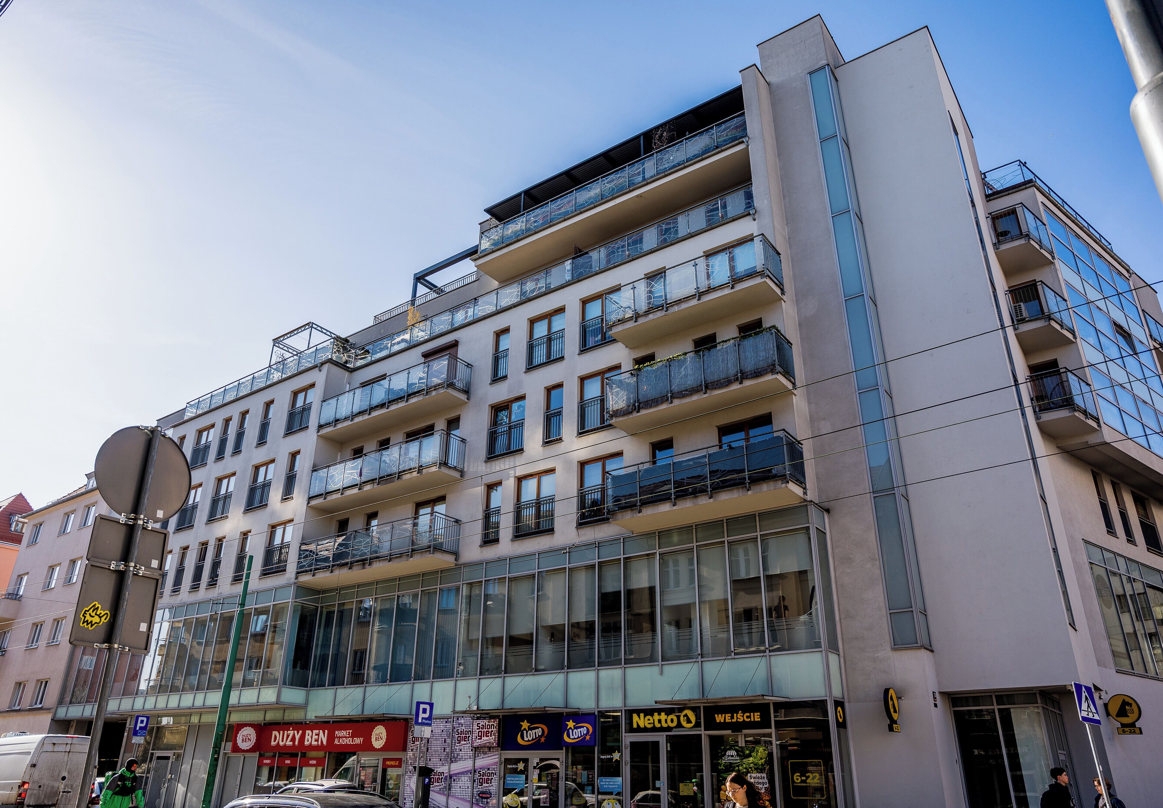 A multi-story building with balconies, large windows, and various storefronts including a Netto supermarket.