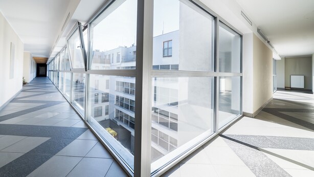 A corridor with large windows, tiled flooring, and a view of buildings outside.