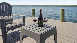 A table with a bottle of wine and two glasses on a deck overlooking a body of water. - Mott's Lakefront Landing: Dog-Friendly Lakefront Escape on Seneca Lake! (Lodi)