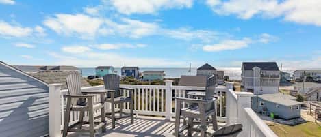 En balkon med stole og udsigt til stranden samt andre bygninger.