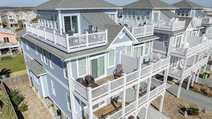 A multi-story beachfront property with balconies, a covered deck, and a sandy driveway. - Sandy Bottoms by Carolina Getaway: Elevator Home w/ Ocean Views & Steps to Beach (Surf City)