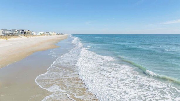 A beach with a clear sky, calm sea, and houses along the shore. - Sandy Bottoms by Carolina Getaway: Elevator Home w/ Ocean Views & Steps to Beach (Surf City)