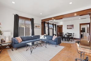 A spacious living room with a blue sectional sofa, a glass coffee table, and a dining area with a table and chairs.