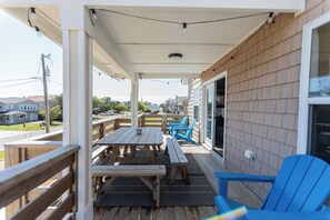 Eine überdachte Terrasse mit Holztischen und blauen Stühlen, ein Holzdeck und Blick auf die Nachbarhäuser.
