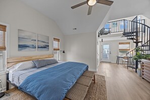 Ein Schlafzimmer mit Bett, Deckenventilator und einer Treppe zu einer oberen Ebene.