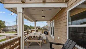 Un patio al aire libre techado con mesas y bancos de madera, una silla negra y luces colgantes.
