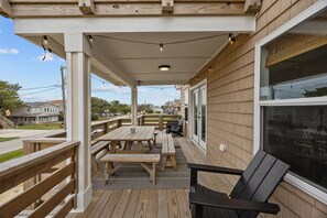 Eine überdachte Terrasse im Freien mit Holztischen und -bänken, einem schwarzen Stuhl und Lichterketten.