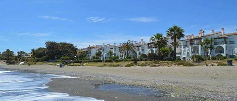 A beachfront hotel with multiple-story buildings, palm trees, and a sandy beach.