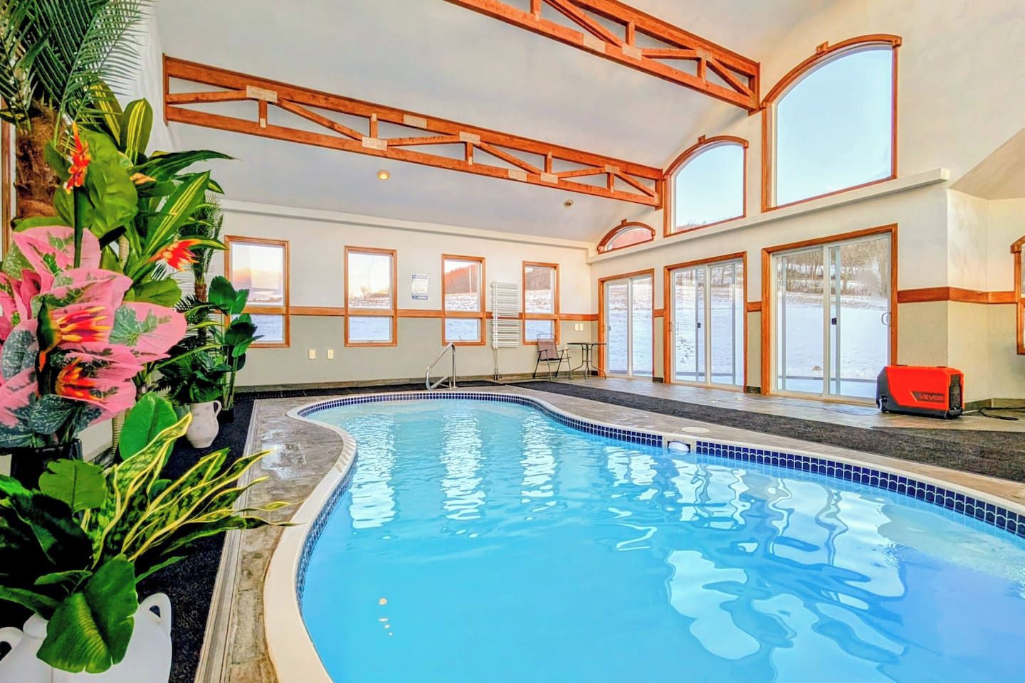 Une piscine intérieure à l’eau d’un bleu cristallin, entourée de grandes fenêtres et de poutres en bois.