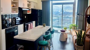 Eine moderne Küche mit einer zentralen Kochinsel, Barhocker und Blick auf eine Stadtlandschaft durch große Fenster.