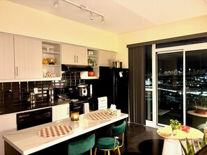 A modern kitchen with a central island, black appliances, and a city view through large windows. - City View Toronto Condo/Leaside (Toronto)