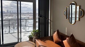 Ein modernes Wohnzimmer mit großem Fenster, einer Couch, einem Spiegel und Blick auf eine verschneite Stadtlandschaft.