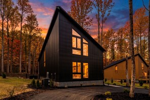 A modern two-story cabin with a steep gable roof, large windows, and a stone foundation. - Fall Getaway~Pickleball~Pool/Sauna~Firepit~Smokies (Pittman Center)