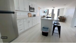 Una cocina moderna con armarios blancos, un microondas y un lavamanos. Hay un cubo de basura y un taburete cerca del lavamanos.