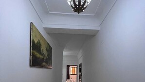 Un pasillo con piso de diseño geométrico, un cuadro en la pared izquierda y una lámpara colgante.