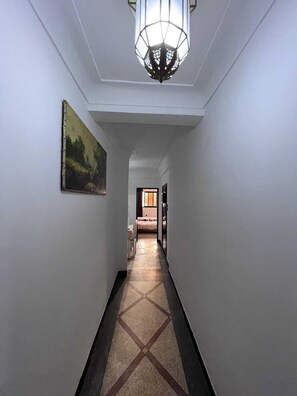 Ein Flur mit einem geometrischen Fußbodenmuster, einem Gemälde an der linken Wand und einer Pendelleuchte.