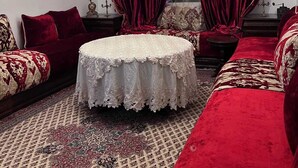 Una habitación con una mesa redonda, sofás de terciopelo rojo, una araña y alfombras estampadas.