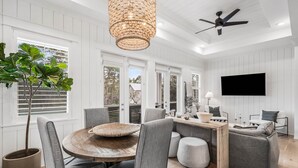 A dining area with a round wooden table, grey upholstered chairs, a woven centerpiece, and a large potted plant. - Stylish 2BR with Community Pools, Golf Cart & Steps to The Big Chill (Inlet Beach)