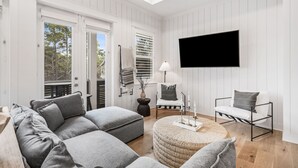 Ein modernes Wohnzimmer mit einer Eckcouch, einem runden Hocker, einem Stuhl mit Metallgestell und einem flachbildfernseher an der Wand.