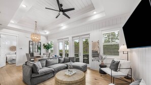 Ein geräumiges Wohnzimmer mit einem grauen Ecksofa, einem runden Hocker und einer schwarzen Stehlampe.