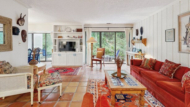 A spacious living room with a red sofa, white wicker furniture, and a large window offering a view of greenery. - Colorful 3-Bedroom Dog-Friendly Condo Near the Ocean, Fernandina Beach (Fernandina Beach)