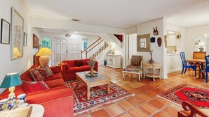 A spacious living room with a red sofa, a coffee table, and a dining area with blue chairs. - Colorful 3-Bedroom Dog-Friendly Condo Near the Ocean, Fernandina Beach (Fernandina Beach)