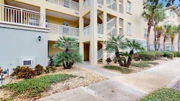 A multi-story building with balconies, palm trees, and a landscaped garden.