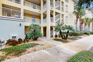 A multi-story building with balconies, palm trees, and a landscaped garden. - Ground floor waterview condo with resort amenities, private patio and pool (Palm Coast)
