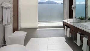 Uma casa de banho moderna com sanita, lavatório e um espelho grande. Vê-se o mar pela janela.