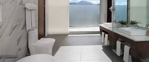 Ein modernes Badezimmer mit Toilette, Waschbecken und einem großen Spiegel. Durch das Fenster ist Meerblick.