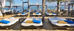 Ein Strandhotel mit mehreren Liegen, die in Reihen angeordnet sind, jeweils mit Sonnendach und Kissen.
