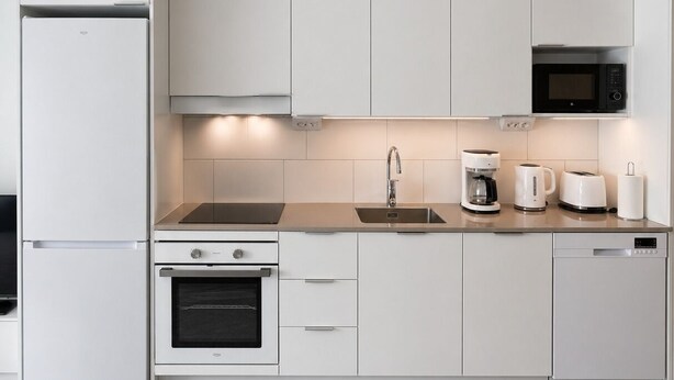 Una cocina moderna con armarios blancos, horno empotrado, microondas, cafetera y pileta.