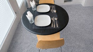 Una mesa de comedor con dos platos blancos, cubiertos y servilletas sobre un mantel oscuro.