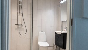 Un baño con ducha de vidrio, inodoro blanco y tocador negro con espejo.