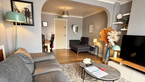 A modern living room with a grey sofa, a coffee table, a TV, and a decorative vase.