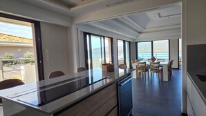 Une cuisine moderne dotée d’un grand îlot central, d’un coin repas avec des chaises et offrant une vue sur la mer grâce à de grandes fenêtres.