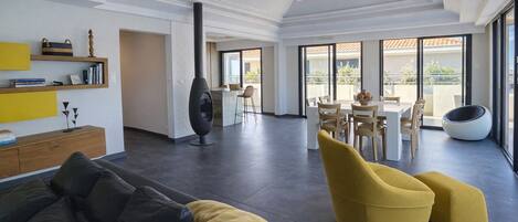A spacious living area with a modern sofa, yellow ottoman, and a dining table with chairs. A unique black spherical chair is visible in the background.