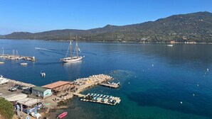 Un port de plaisance avec des bateaux amarrés, un voilier sur l’eau et une chaîne de montagnes en arrière-plan.