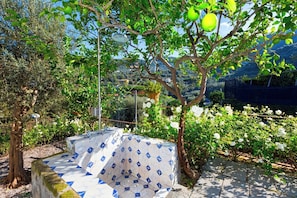 A covered outdoor seating area with a tiled floor, surrounded by greenery and flowering plants. - Villa Giardino Segreto, Close to Sorrento (Sorrento)