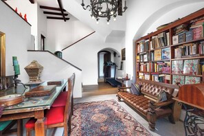 Ein geräumiges Wohnzimmer mit einer großen Bücherwand, einem Ledersofa und einem Essbereich mit einem Glastisch und Stühlen.