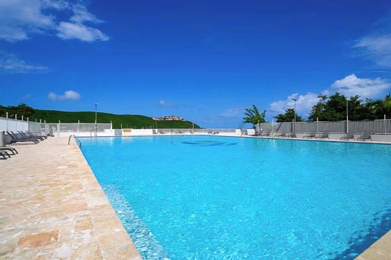 En klar, blå swimmingpool med liggestole og en terrasse med sten.