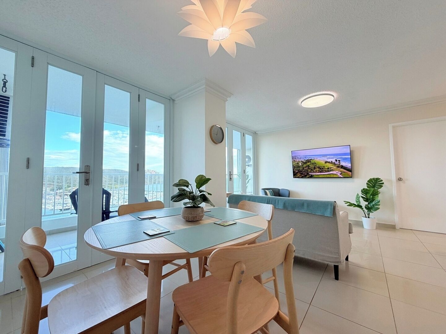 A modern dining area with a round table, chairs, and a view of the sea through large windows.