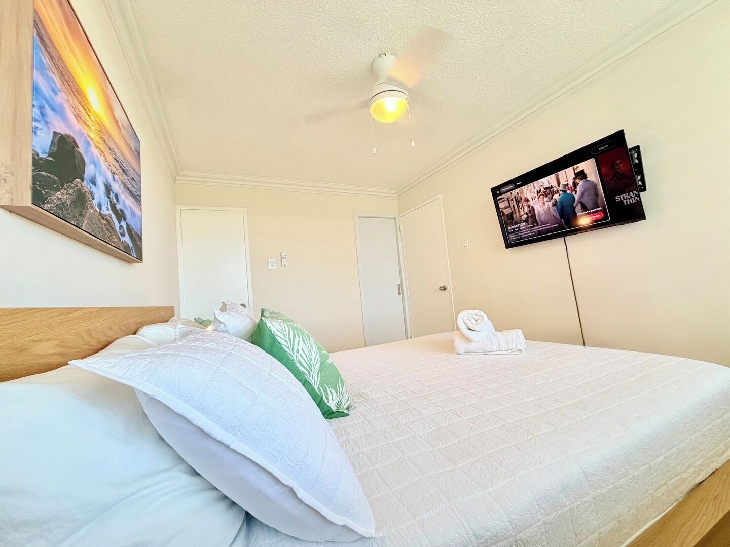 A hotel room with two beds, a television mounted on the wall, and a painting on the wall.