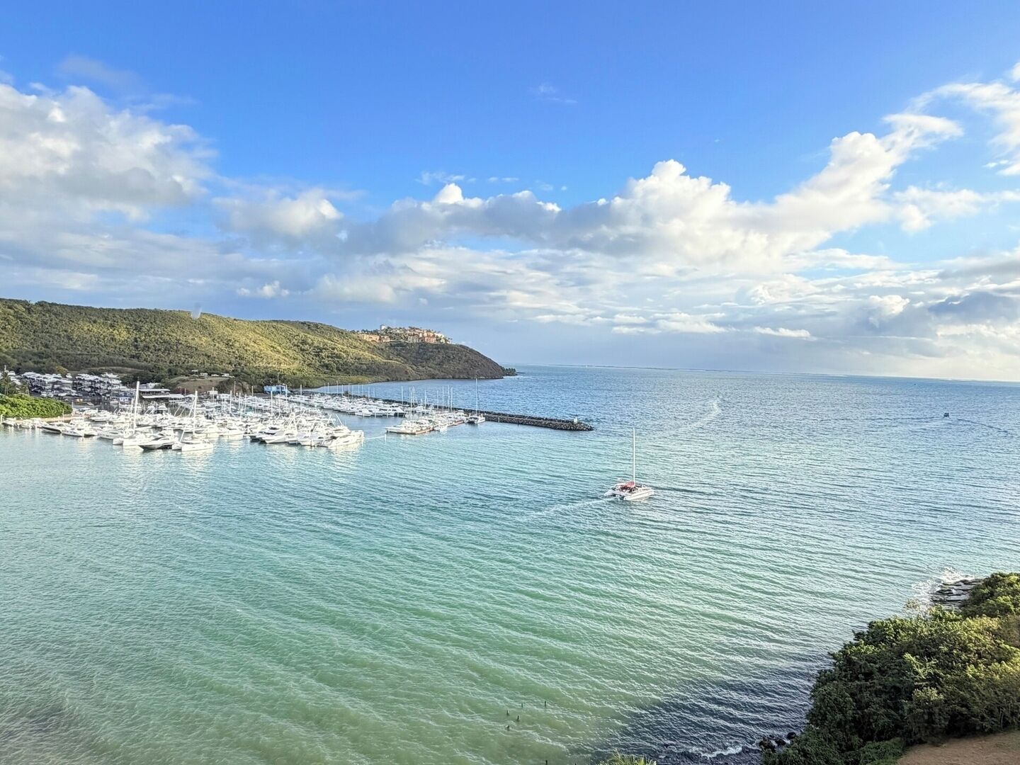 A marina with boats docked, a clear sky, and a hilly landscape in the background.