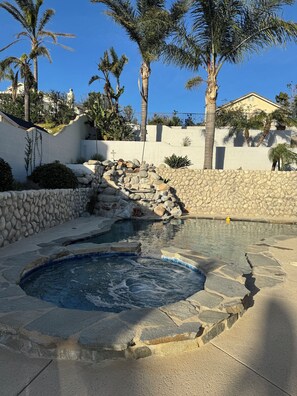 A hot tub surrounded by a stone wall, palm trees, and a clear blue sky. - Private Pool Oasis • Relaxation & Comfort (San Bernardino)