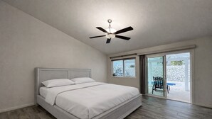 Un dormitorio con cama, ventilador de techo y puerta corrediza de vidrio que da a un espacio exterior.