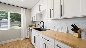Una cocina moderna con armarios blancos, un lavamanos negro y una encimera de madera.